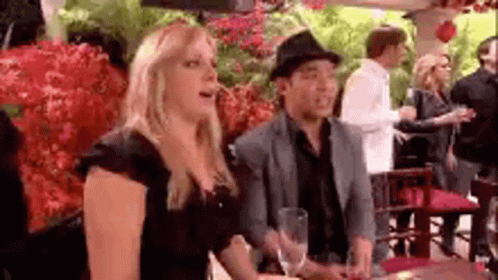 A Man And A Woman Are Sitting At A Table In A Restaurant . The Woman Is Wearing A Hat . GIF