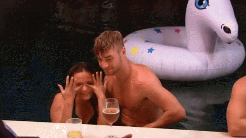 A Man And A Woman Are Sitting At A Table In Front Of An Inflatable Unicorn . GIF