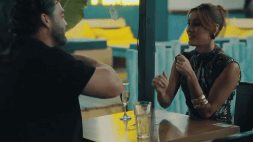 A Man And A Woman Are Sitting At A Table Talking To Each Other . GIF