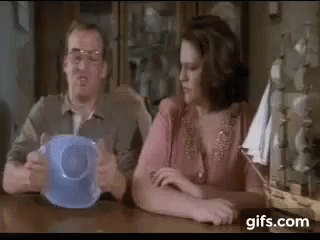 A Man And A Woman Are Sitting At A Table With A Blue Cup . GIF