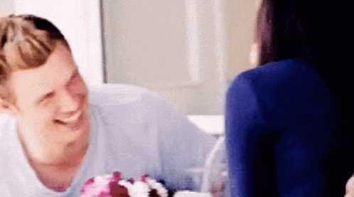 A Man And A Woman Are Sitting At A Table With A Cake On It . GIF