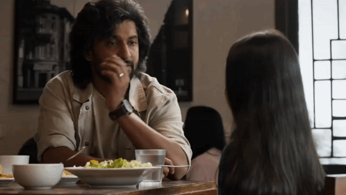 A Man And A Woman Are Sitting At A Table With A Plate Of Food GIF