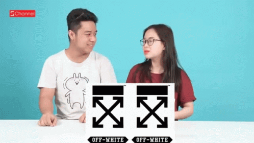 A Man And A Woman Are Sitting At A Table With A Sign That Says Off White GIF