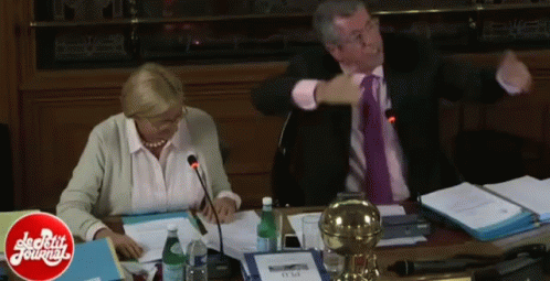 A Man And A Woman Are Sitting At A Table With A Sign That Says ' Strictly Journals ' On It GIF
