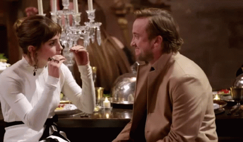 A Man And A Woman Are Sitting At A Table With Candles On It GIF