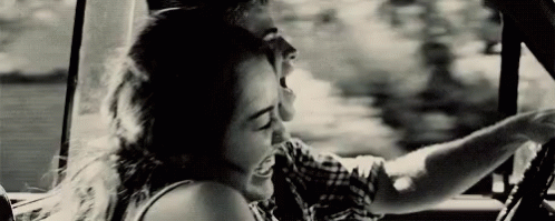 A Man And A Woman Are Sitting In A Car And Laughing . GIF