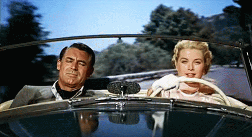 A Man And A Woman Are Sitting In A Car Looking At Each Other GIF