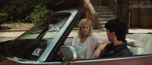 A Man And A Woman Are Sitting In A Car With A Sticker That Says S On It GIF