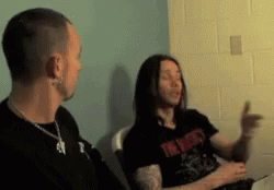 a man and a woman are sitting in a room and the man is wearing a black shirt that says ' i '