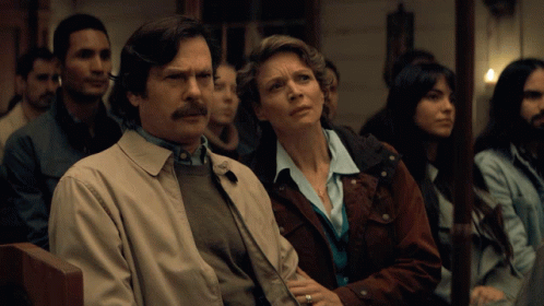A Man And A Woman Are Sitting In A Row Of People GIF