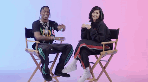 A Man And A Woman Are Sitting In Directors Chairs And Smiling GIF