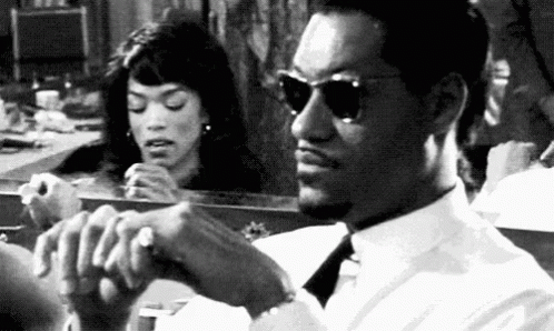 A Man And A Woman Are Sitting In Front Of A Mirror . The Man Is Wearing Sunglasses . GIF