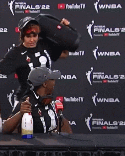 A Man And A Woman Are Sitting In Front Of A Wall That Says Wnba Finals 22 GIF