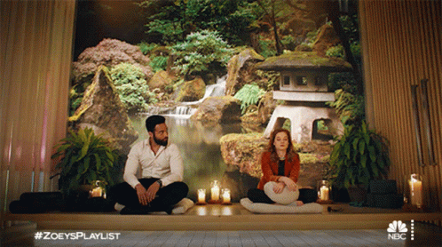 A Man And A Woman Are Sitting In Front Of A Wall With A Waterfall In The Background GIF