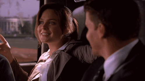 A Man And A Woman Are Sitting In The Back Seat Of A Car And The Woman Is Smiling GIF