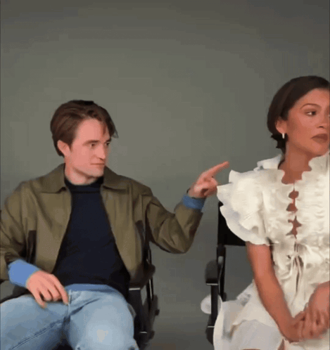 A Man And A Woman Are Sitting Next To Each Other And The Woman Is Pointing At The Man GIF