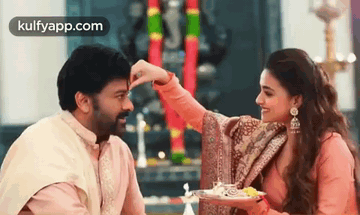 A Man And A Woman Are Sitting Next To Each Other And The Woman Is Putting Something On The Man 'S Face . GIF