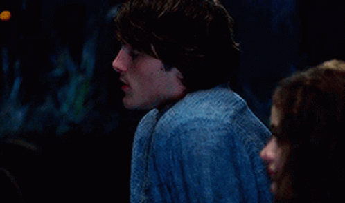 A Man And A Woman Are Sitting Next To Each Other In A Dark Room . The Man Is Wearing A Blue Shirt . GIF