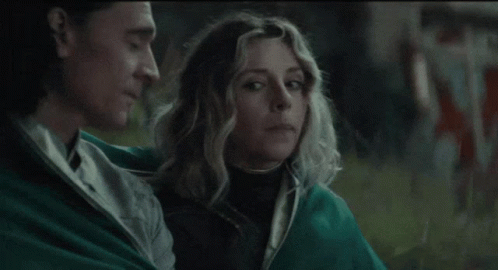 A Man And A Woman Are Sitting Next To Each Other In A Field . GIF