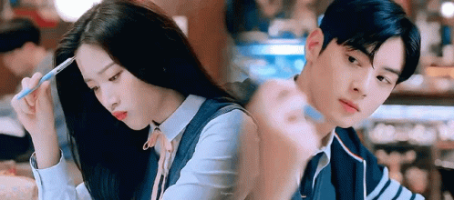A Man And A Woman Are Sitting Next To Each Other In A Restaurant . The Woman Is Holding A Pen In Her Hand . GIF