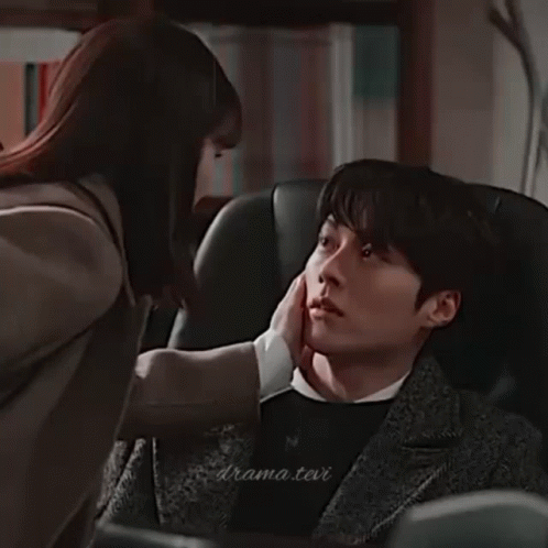 A Man And A Woman Are Sitting Next To Each Other In A Room And Looking At Each Other . GIF