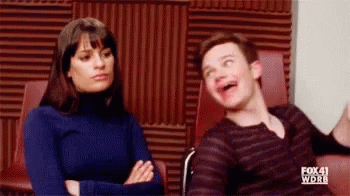 A Man And A Woman Are Sitting Next To Each Other In A Room . The Man Is Making A Funny Face . GIF