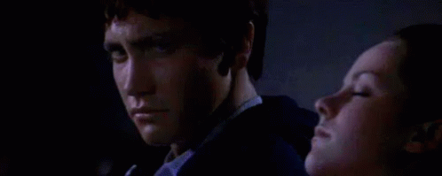 A Man And A Woman Are Sitting Next To Each Other In The Dark . GIF