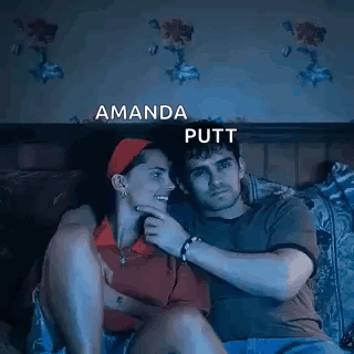 A Man And A Woman Are Sitting Next To Each Other On A Bed Watching A Movie . GIF
