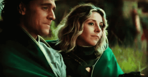 A Man And A Woman Are Sitting Next To Each Other On A Blanket . GIF