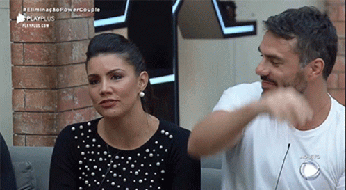 A Man And A Woman Are Sitting Next To Each Other On A Couch And The Man Is Pointing At The Woman . GIF