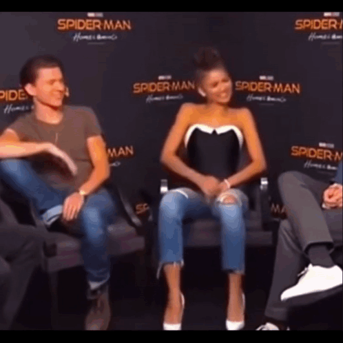 A Man And A Woman Are Sitting Next To Each Other On A Couch In Front Of A Spider Man Sign . GIF