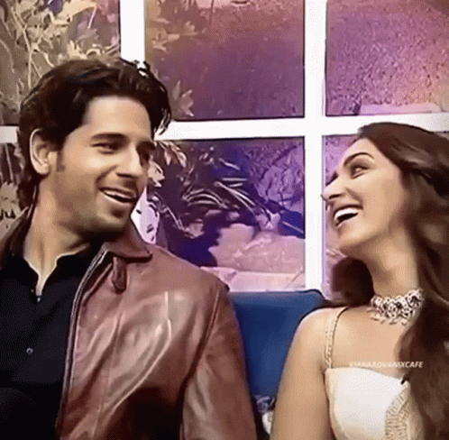 A Man And A Woman Are Sitting Next To Each Other On A Couch Laughing . GIF