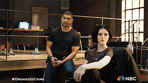 A Man And A Woman Are Sitting Next To Each Other With A Nbc Logo In The Background GIF