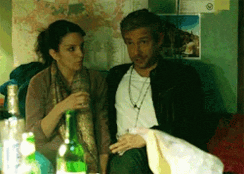 A Man And A Woman Are Sitting Next To Each Other With Bottles Of Alcohol In Front Of Them GIF