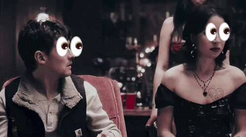 A Man And A Woman Are Sitting Next To Each Other With Cartoon Eyes On Their Faces GIF