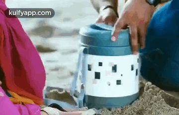 A Man And A Woman Are Sitting On A Beach Holding A Thermos . GIF