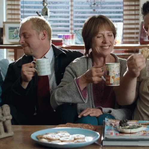 A Man And A Woman Are Sitting On A Couch Drinking Coffee And Smiling GIF