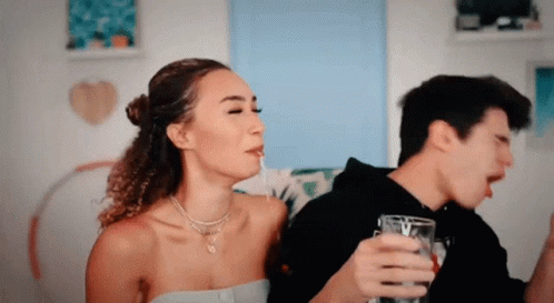 A Man And A Woman Are Sitting On A Couch Drinking From Glasses GIF