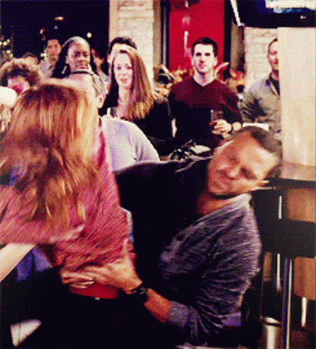 A Man And A Woman Are Sitting On A Couch In Front Of A Crowd Of People GIF