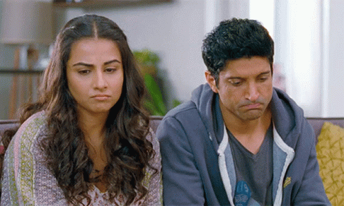 A Man And A Woman Are Sitting On A Couch With Their Faces Turned Towards The Camera GIF