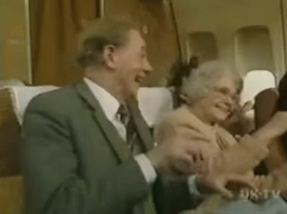 A Man And A Woman Are Sitting On A Plane Laughing And Hugging Each Other . GIF