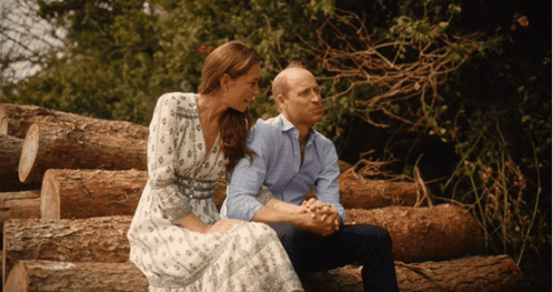 A Man And A Woman Are Sitting On Logs Holding Hands GIF
