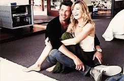 A Man And A Woman Are Sitting On The Floor Hugging Each Other And Smiling . GIF