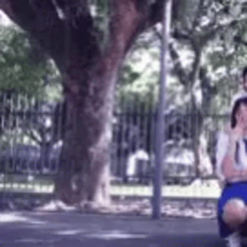 A Man And A Woman Are Sitting Under A Tree On The Side Of The Road . GIF