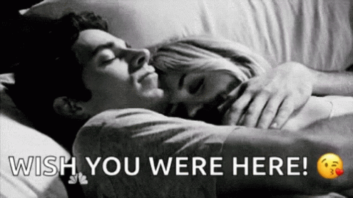 A Man And A Woman Are Sleeping In A Bed With The Words `` Wish You Were Here '' Written Above Them . GIF