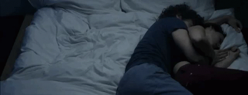 A Man And A Woman Are Sleeping On A Bed With White Sheets GIF