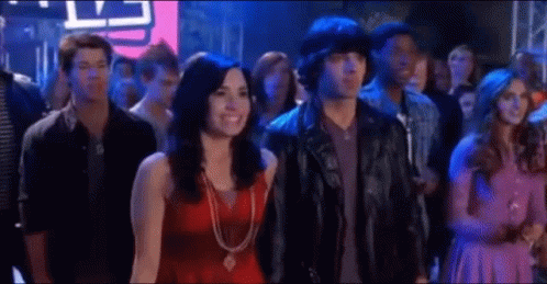 A Man And A Woman Are Standing In A Crowd Of People At A Party . GIF