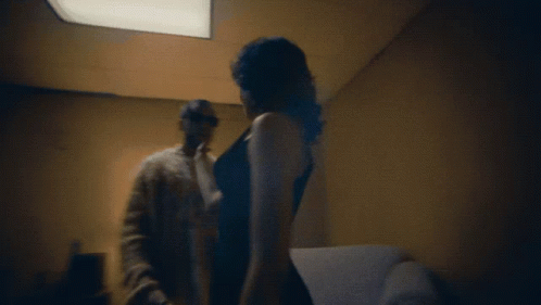 A Man And A Woman Are Standing In A Dark Room GIF