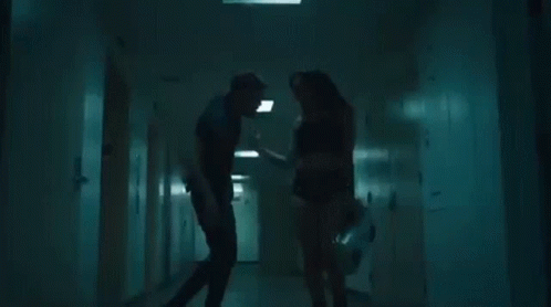 A Man And A Woman Are Standing In A Hallway . GIF