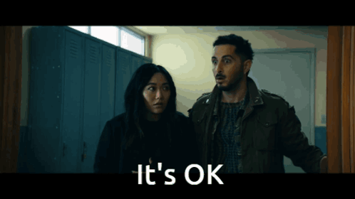 A Man And A Woman Are Standing In A Hallway With The Words " It 'S Ok " On The Bottom GIF